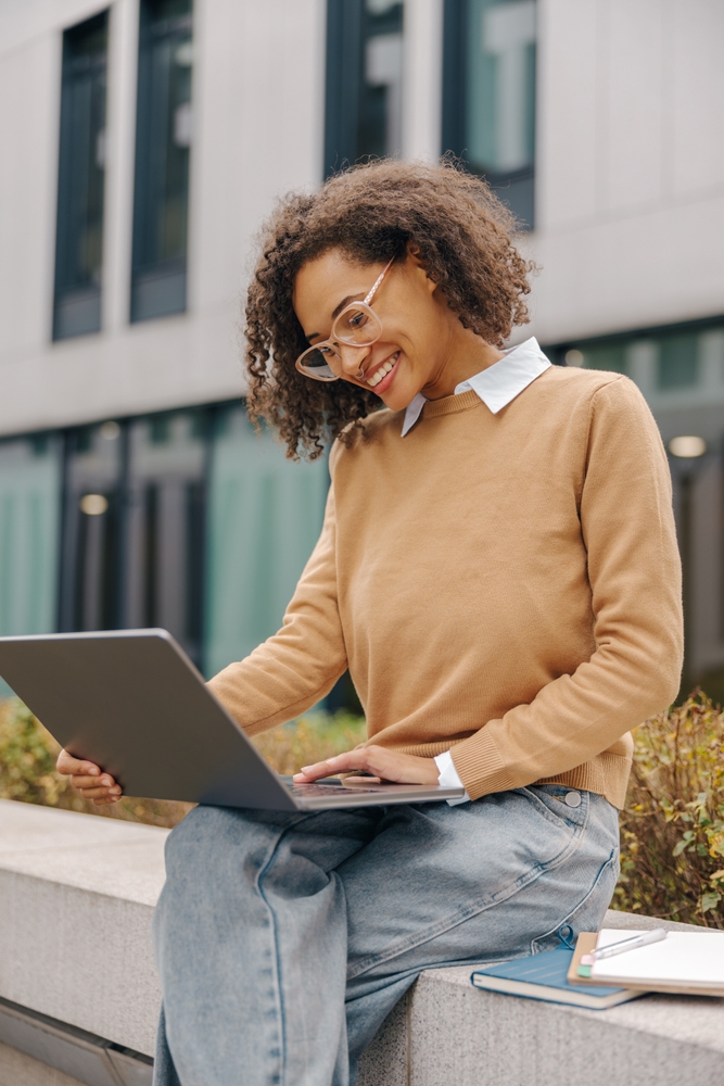 Pretty face female smiling, young entrepreneur is sitting outside with a laptop on her lap, overlooking a complete, full dissertation